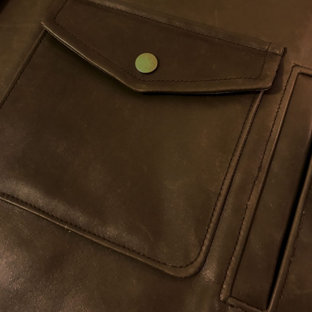 Close-up of a patch pocket with pointed flap and snap closure, with a single-welt pocket opening next to it