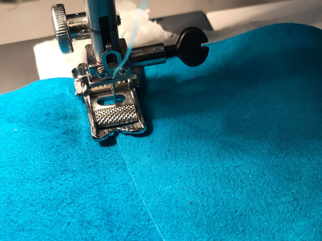 blue pig suede being sewn with a roller foot and tissue underneath